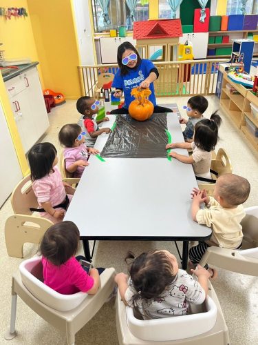 Infants watching teacher carve pumpkin during Halloween celebration at BKMCC North Delta.