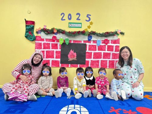 Caring teachers holding Toddlers in front of a handmade fireplace decoration at BKMCC North Delta.
