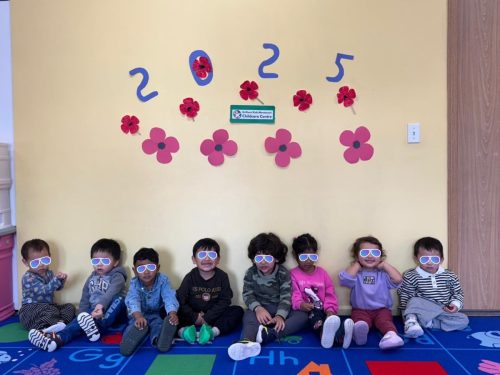 Toddlers at BKMCC Childcare in North Delta sit by a poppy wall for Remembrance Day.